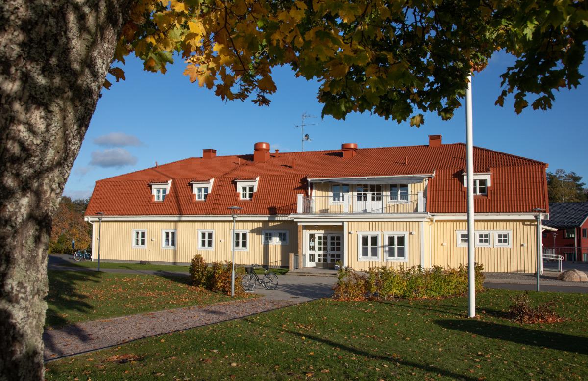 Gult tvåvåningshus med rött tegeltak, inramat av ett träd i höstfärger