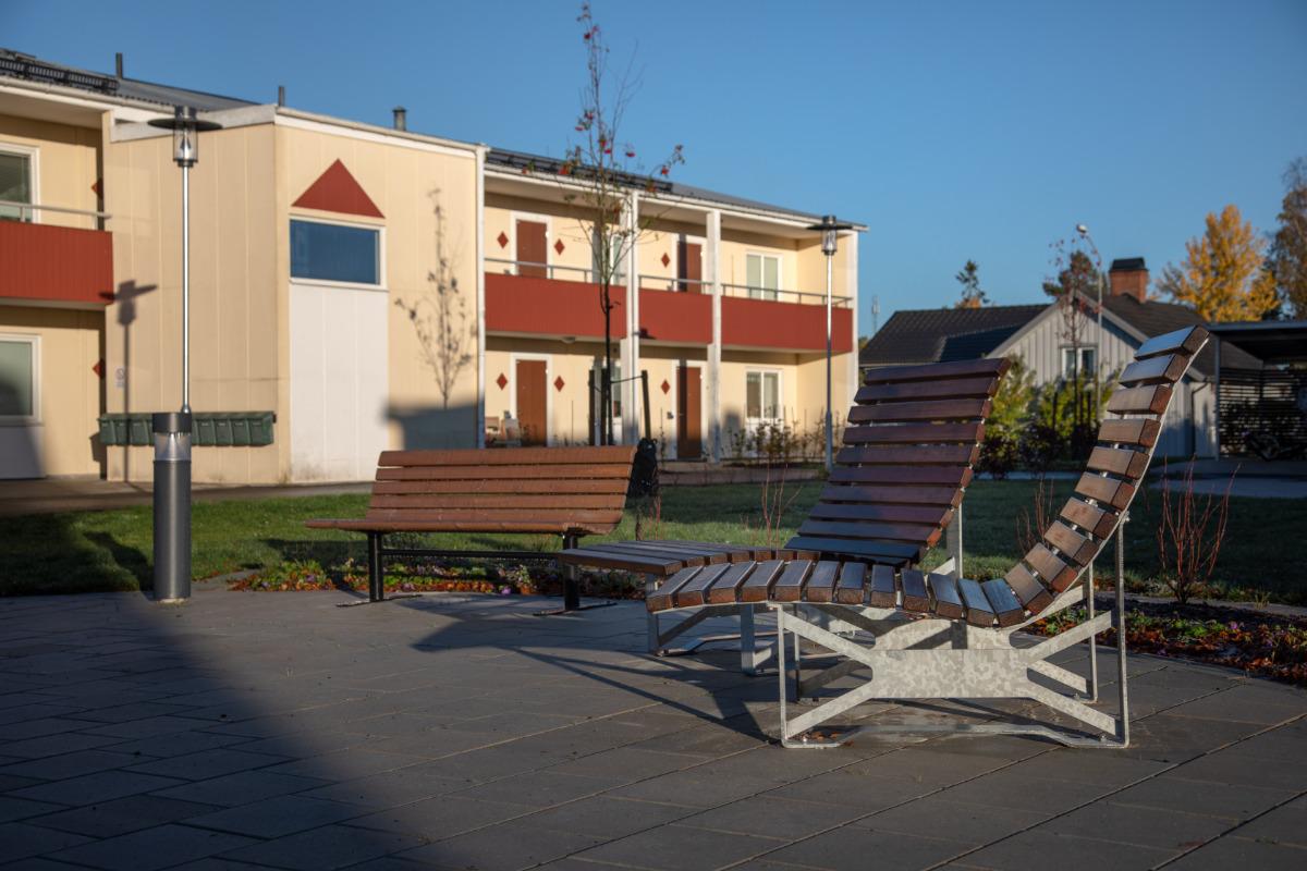 Innergård med bänk och vilstolar i trä framför ett gult tvåvåningshus med röda balkonger